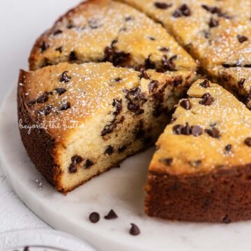 Slices of chocolate chip ricotta cake on a marble cake round with small bowl of mini chocolate chips nearby | © Beyond the Butter®