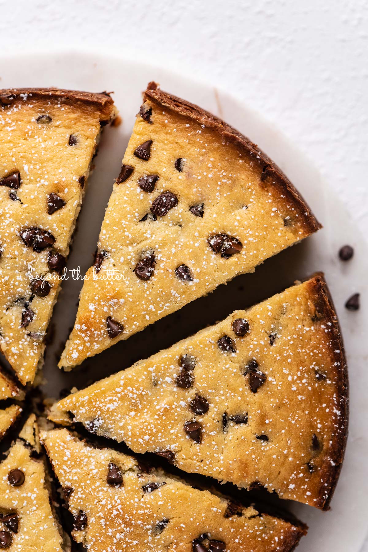 Sliced chocolate chip ricotta cake on a marble cake round with small bowl of mini chocolate chips nearby | © Beyond the Butter®