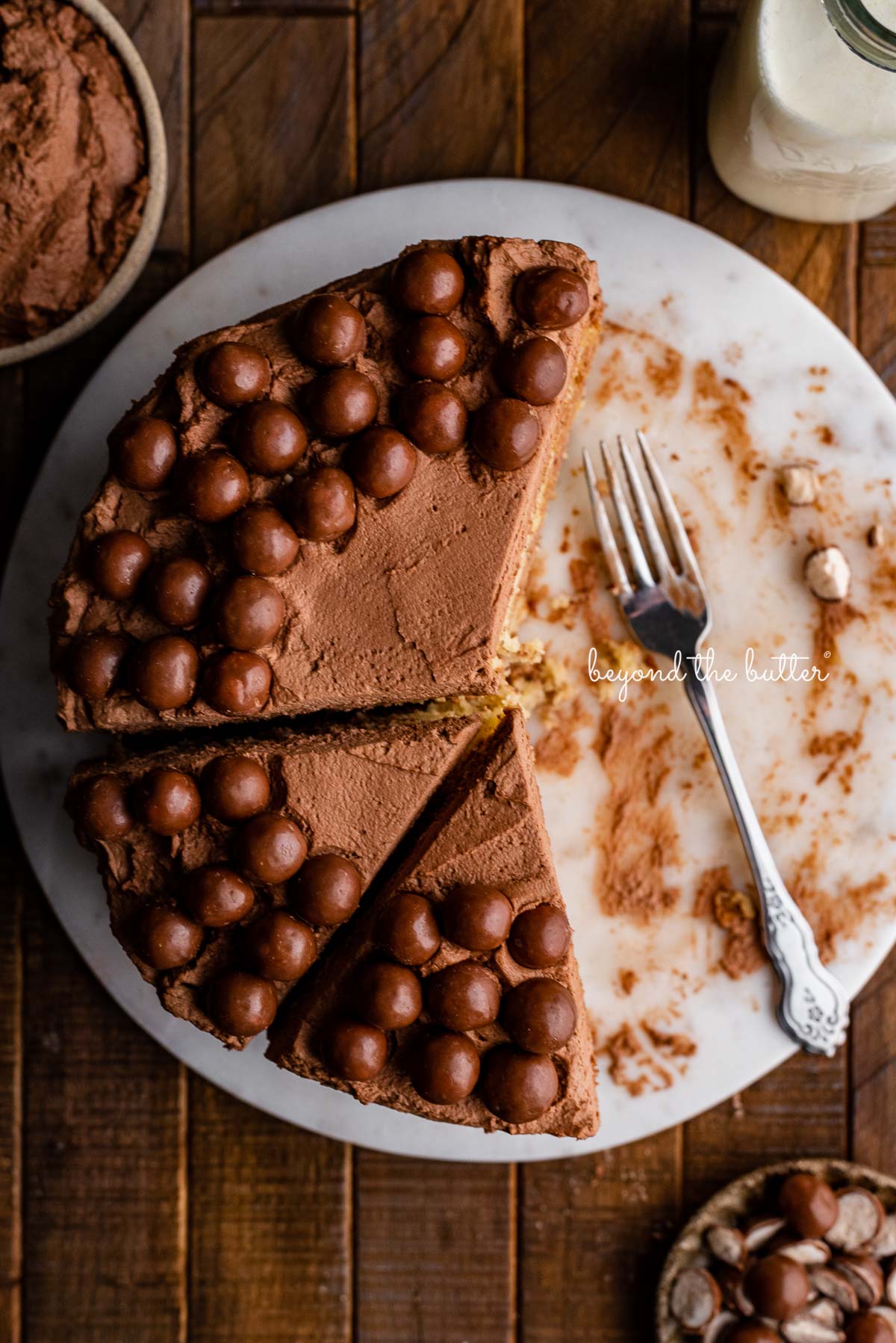 Top down view of 2 layer moist banana cake frosted with malted chocolate mascarpone whipped cream and garnished with malted chocolate balls on marble cake board | © Beyond the Butter®