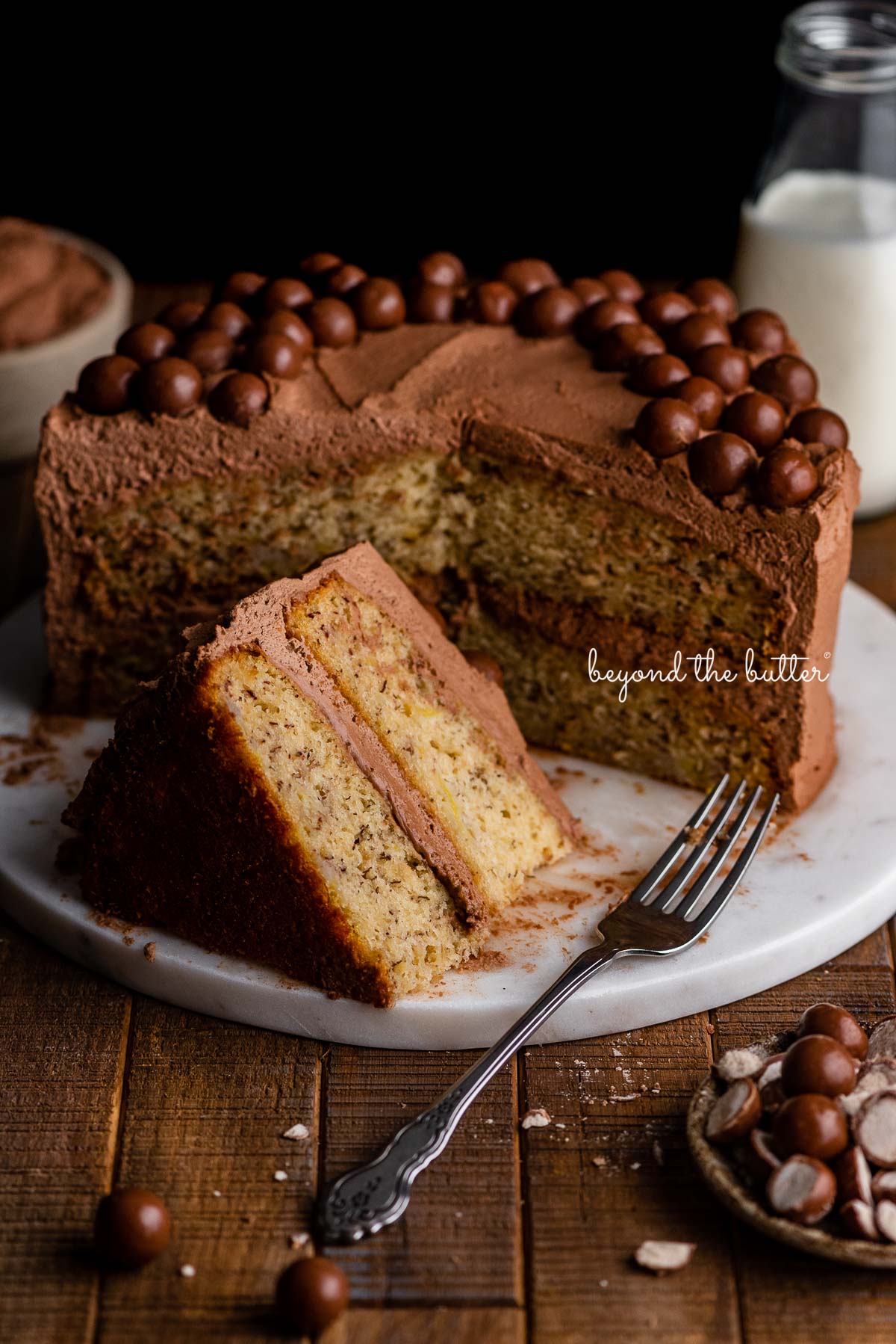 Moist banana cake with slices cut out on marble cake board and dark wood backround | © Beyond the Butter®