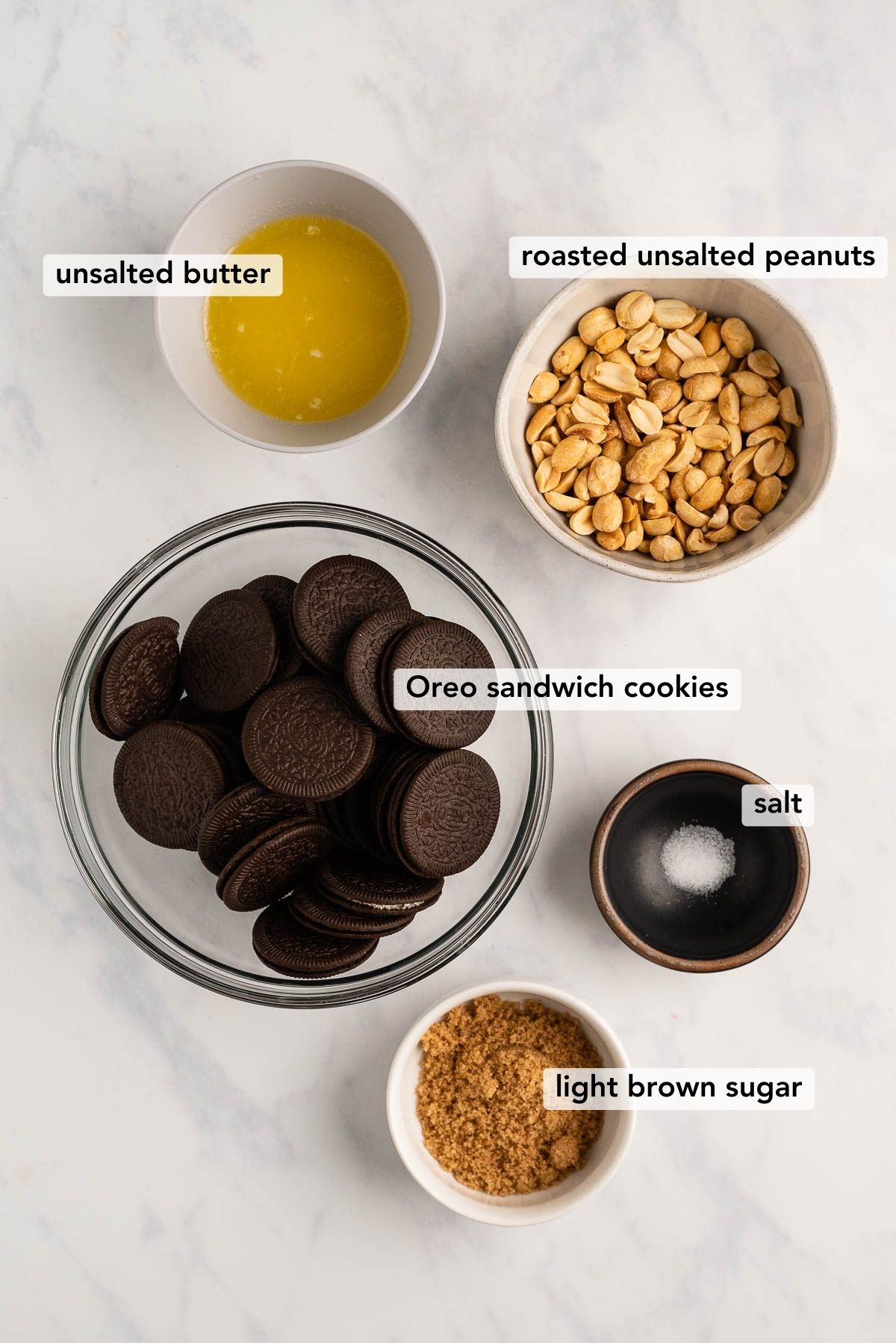 Overhead image of ingredients used to make the oreo cookie crust for a Reese's peanut butter cheesecake on white and grey marble background.