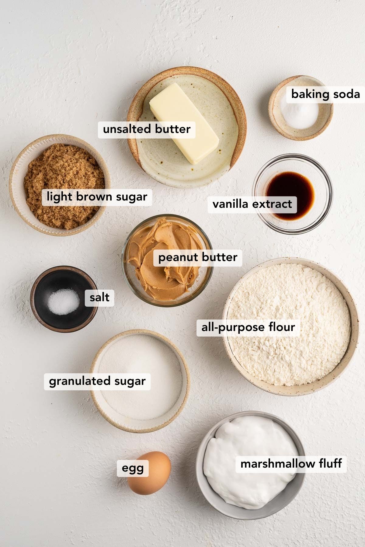 ingredients used to make peanut butter marshmallow cookies, labeled, and on a white textured background.