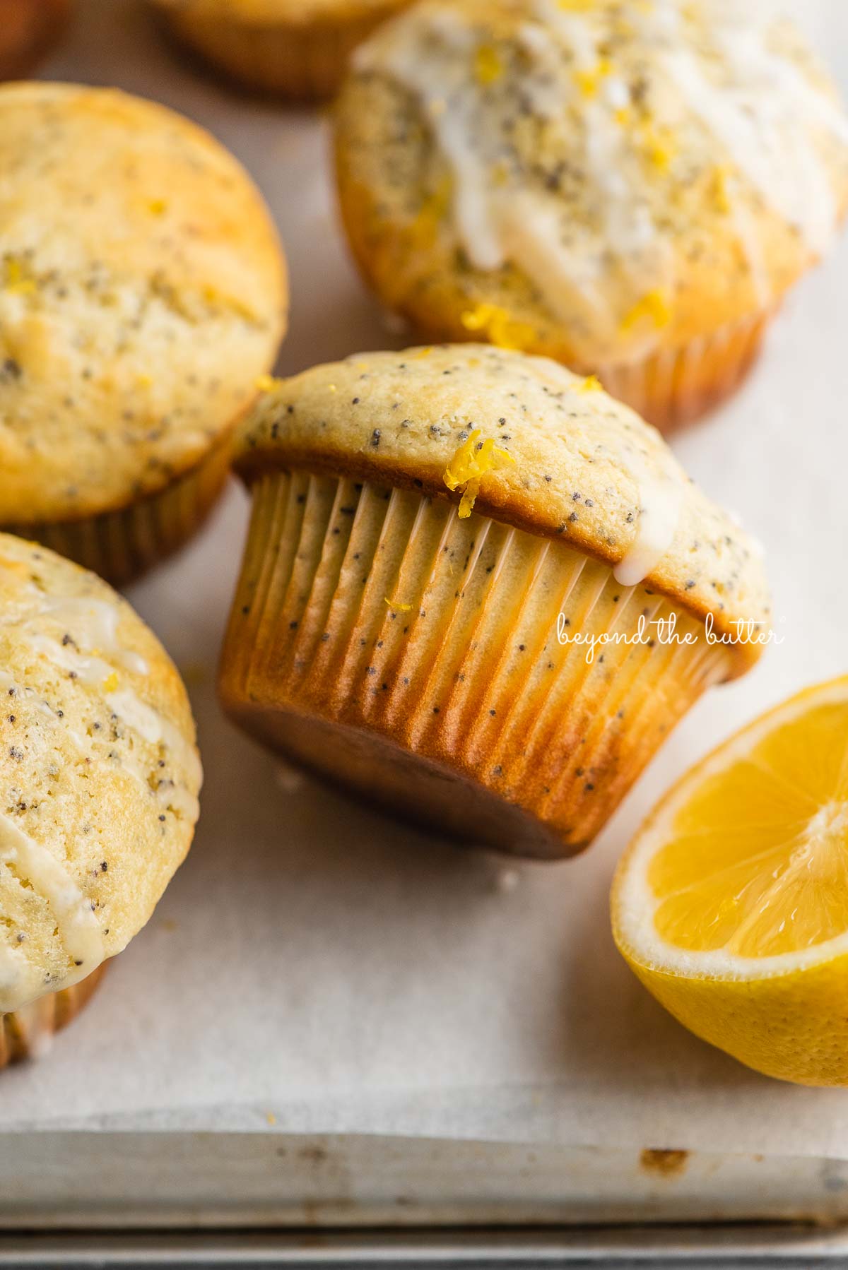 Lemon poppyseed muffins randomly placed on a parchment paper lined baking sheet with half of lemon.