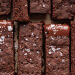 Sliced homemade chocolate shortbread sprinkled with flaky sea salt on natural parchment paper.