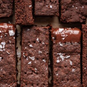 Sliced homemade chocolate shortbread sprinkled with flaky sea salt on natural parchment paper.