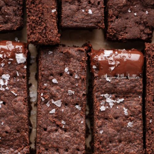 Sliced homemade chocolate shortbread sprinkled with flaky sea salt on natural parchment paper.