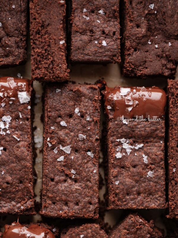 Sliced homemade chocolate shortbread sprinkled with flaky sea salt on natural parchment paper.