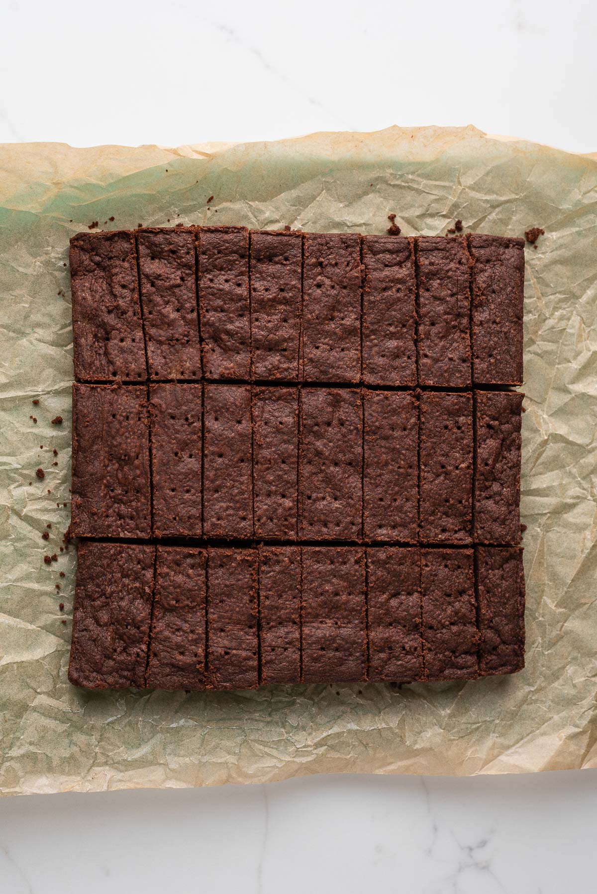 Sliced chocolate shortbread biscuits ted lasso style on a parchment paper lined cutting board and white marbled surface.