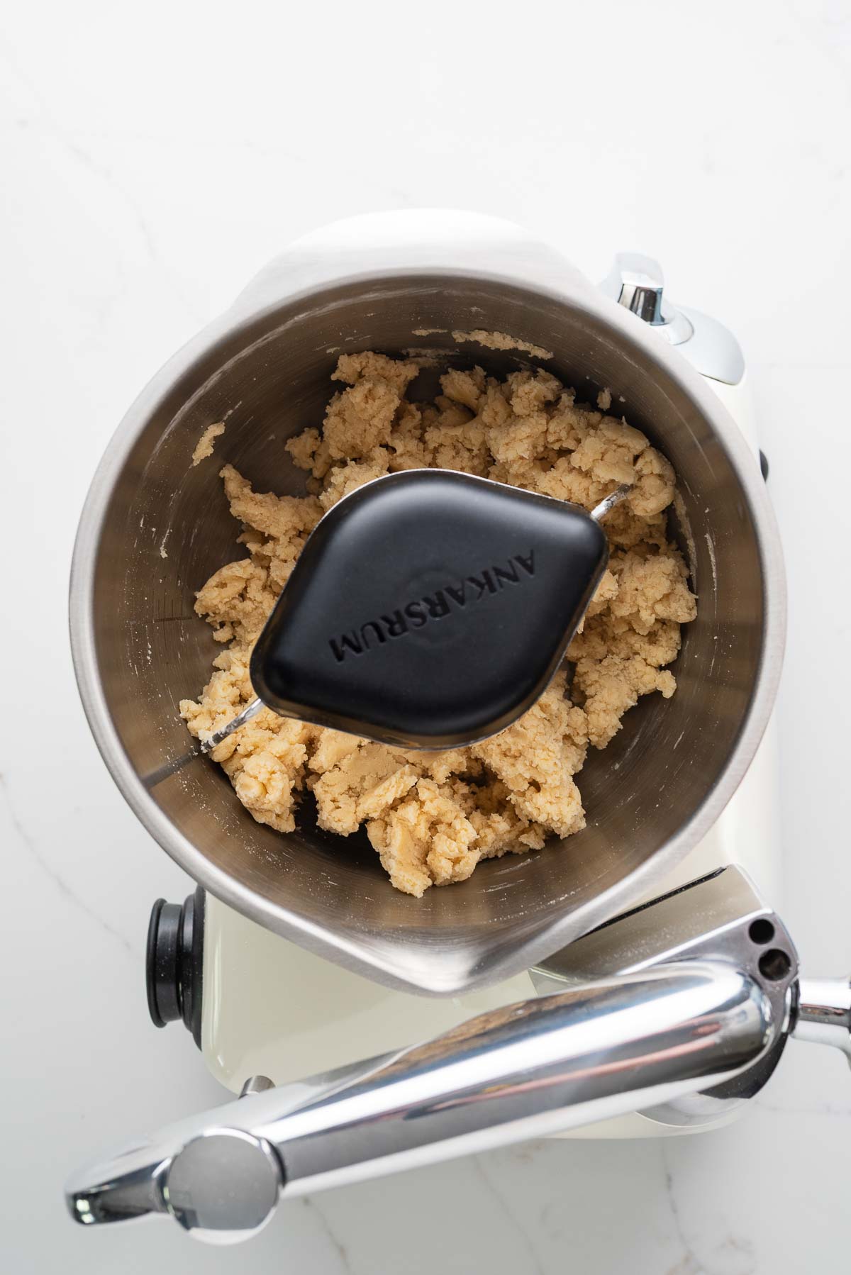 Flour, salt, sugar, cold cubed butter, and ice cold butter mixed together in a creme light colored ankarsrum assistent original mixer and stainless steel beater bowl with their new premium beater set.