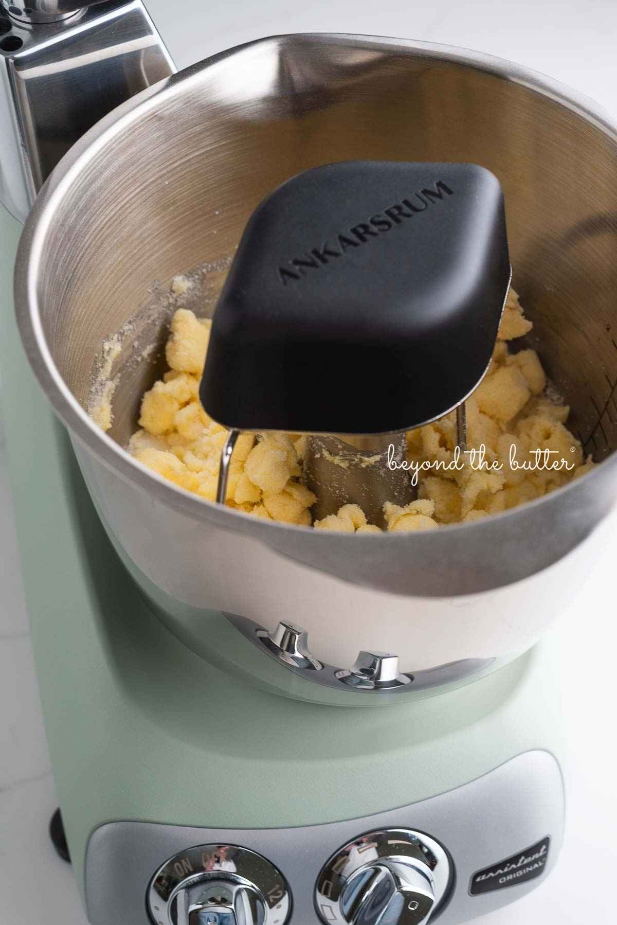 Ankarsrum assistent original mixer in nordic sage mixing butter and sugar together using the premium beater set and cookie whisks.