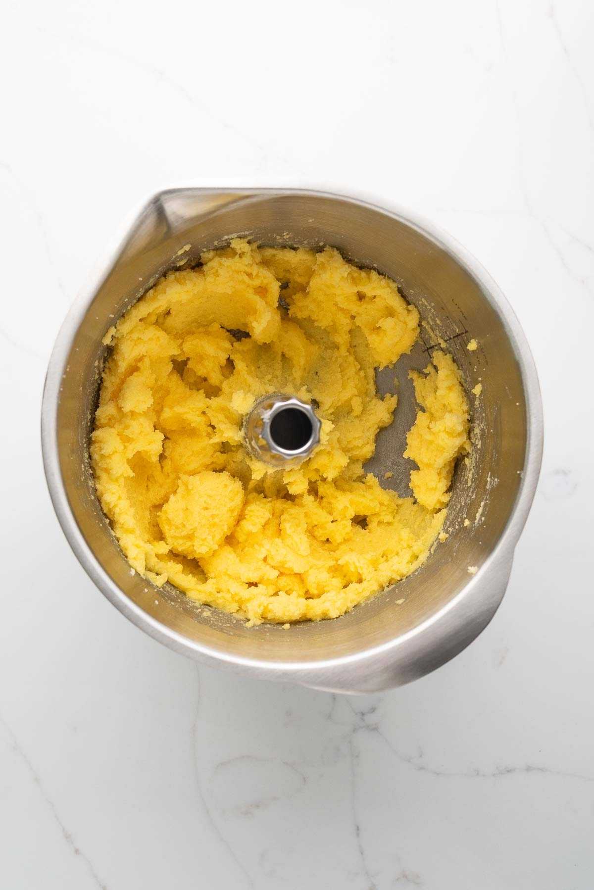 Beaten sugar, butter, and egg yolks in a stainless steel mixing bowl on a white marbled background.