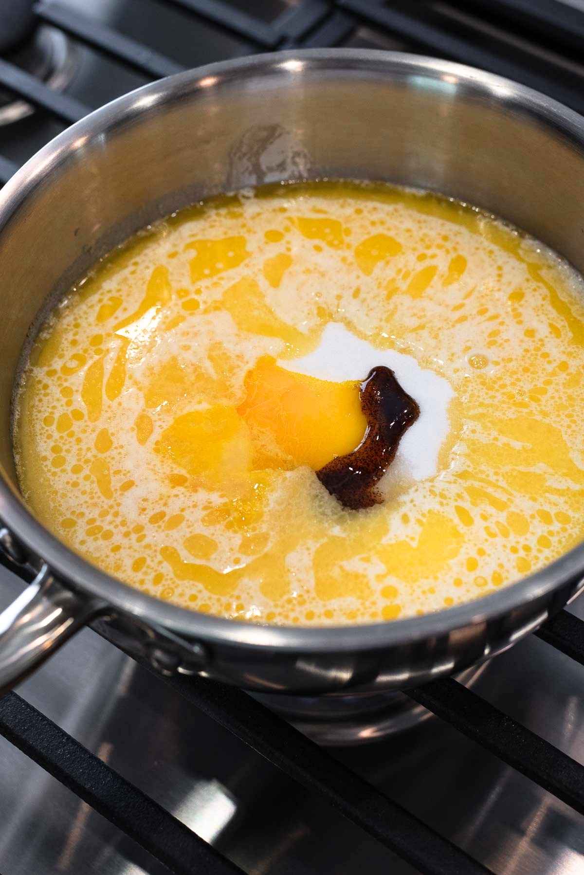 Butter, evaporated milk, sugar, vanilla extract, rum extract, and slightly whisked egg yolks added to a stainless steel saucepan.