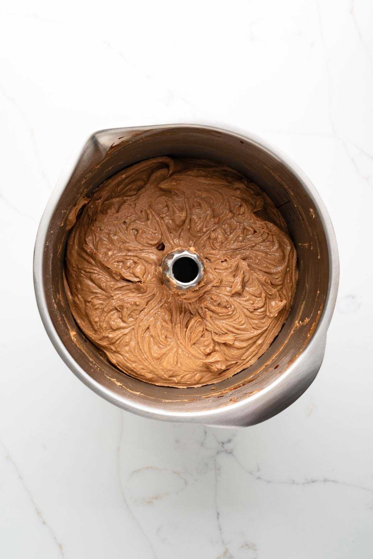 Flour mixture and buttermilk added to the German chocolate cake batter in a stainless steel mixing bowl on a white marbled background.