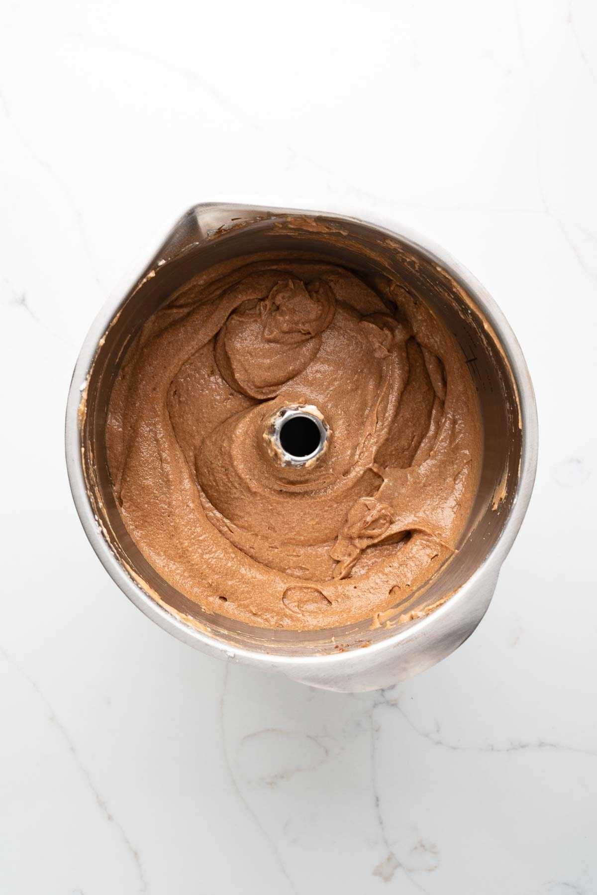 Stiff peak egg whites folded into German chocolate cake batter in a stainless steel mixing bowl on a white marbled background.