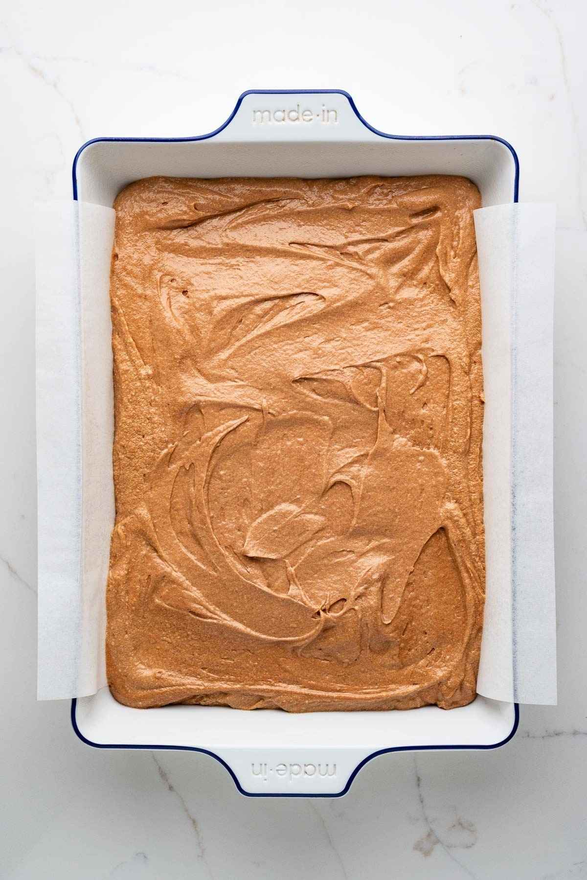 German chocolate cake batter spread into a parchment paper lined ceramic white baking dish.