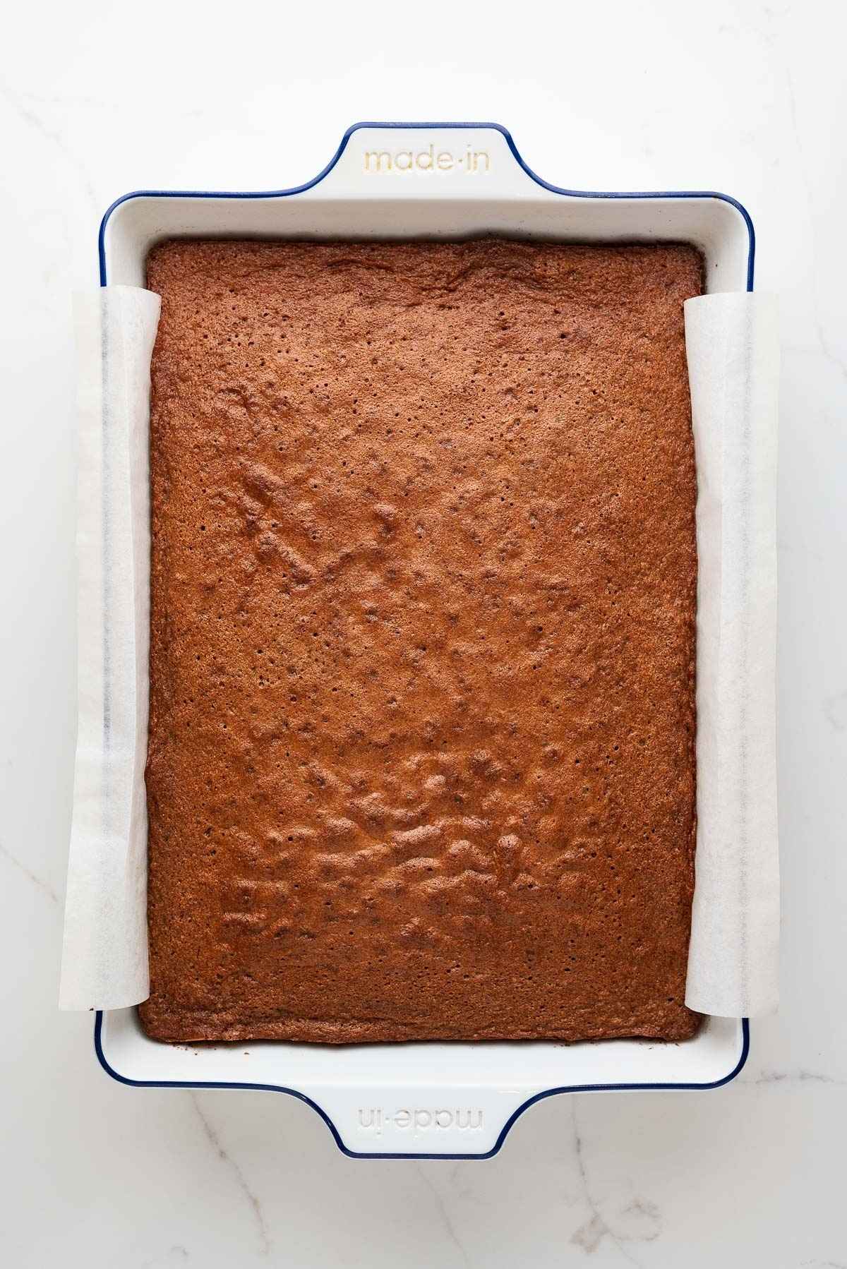 Baked German chocolate sheet cake in a parchment paper lined white ceramic baking dish.