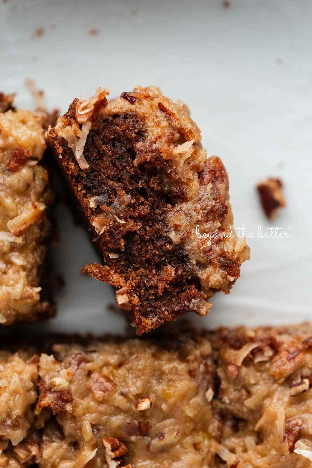 Sliced German chocolate sheet cake on its side next to other slices in a parchment paper lined ceramic baking pan.