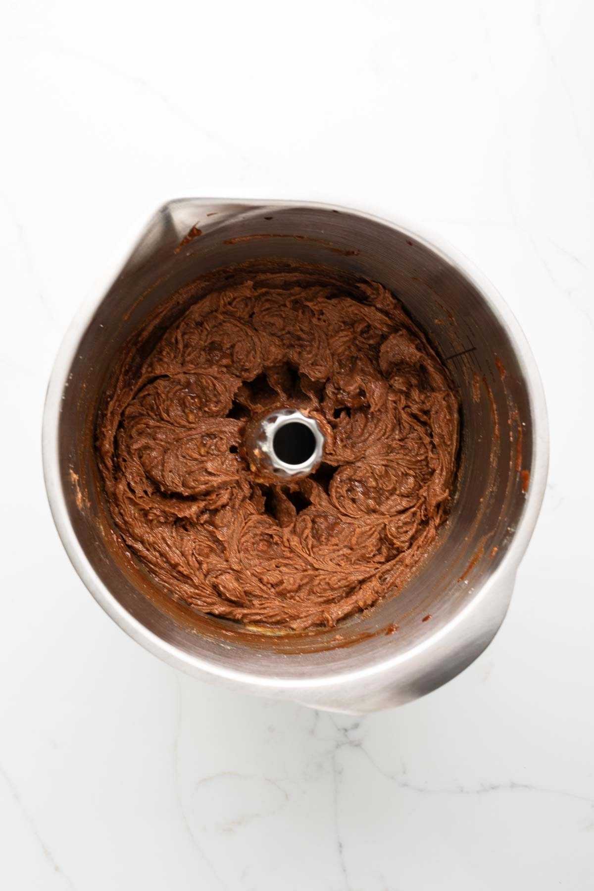 Melted chocolate and vanilla extract mixed into the cake batter in a stainless steel mixing bowl on a white marbled background.