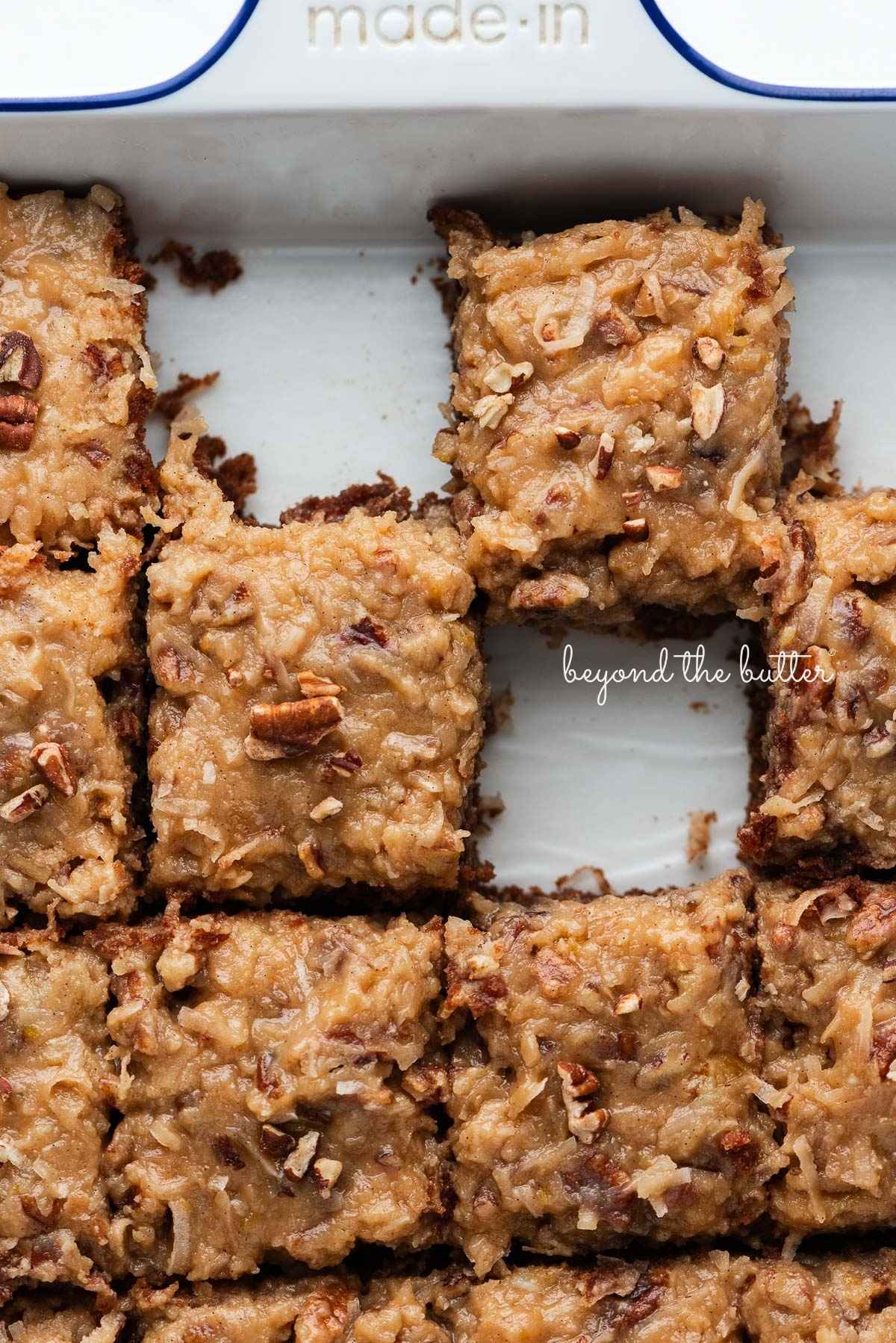 Slices of German chocolate cake in a parchment paper lined ceramic white baking dish.